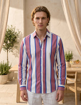 Man wearing a striped shirt standing outdoors with plants and furniture in the background