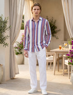 Man wearing a striped shirt and white pants standing outdoors.