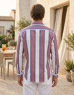 Man wearing a striped shirt standing outdoors with a patio and plants in the background