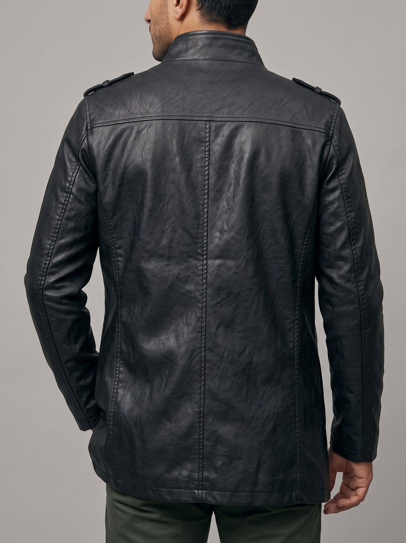 A man viewed from the back wearing a black leather jacket with shoulder epaulets, set against a solid gray studio background.