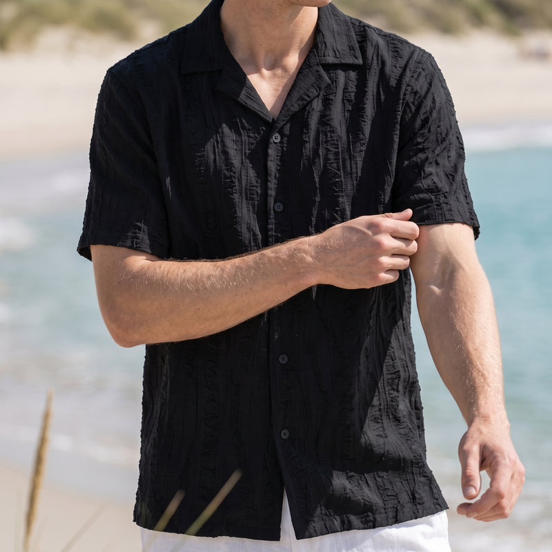 A man wearing a black short-sleeve button-up shirt with a textured crinkled fabric