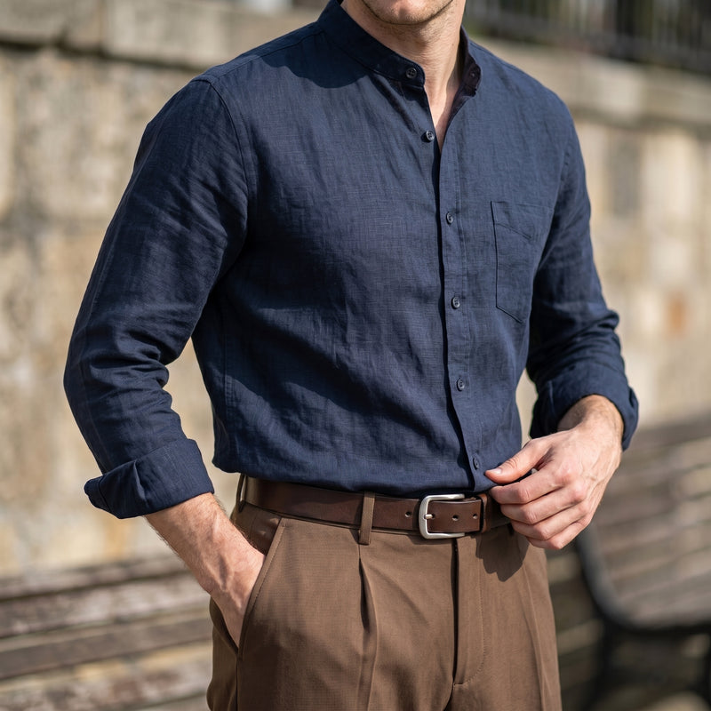 A man wearing a dark navy blue linen long-sleeve button-down shirt tucked into brown trousers with a brown belt