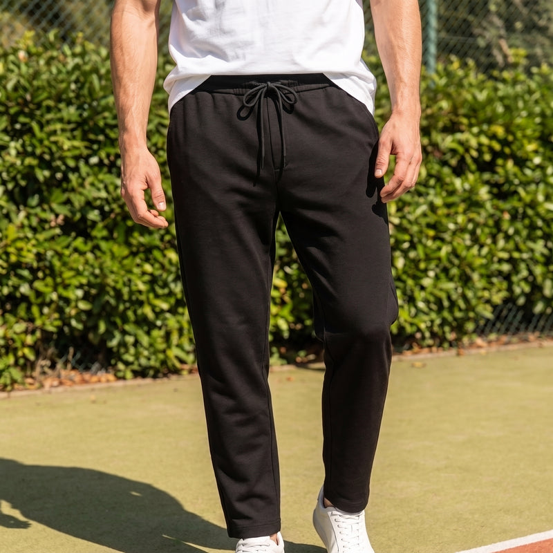 A man wearing black drawstring sweatpants, a white t-shirt, and white sneakers
