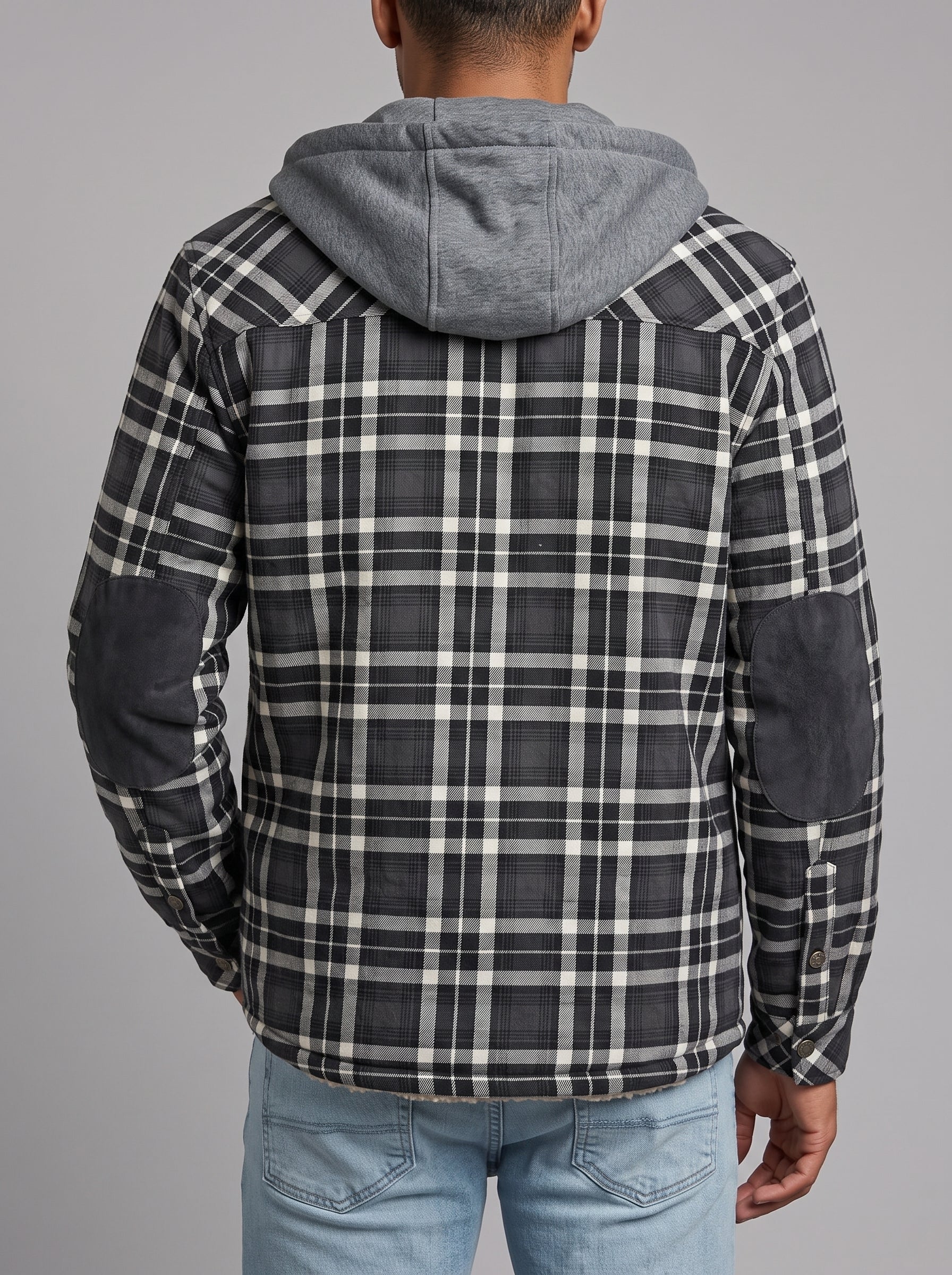 A person shown from the back wearing a hooded jacket with a black, white, and gray plaid pattern and dark gray elbow patches, paired with light blue jeans against a solid gray studio background.