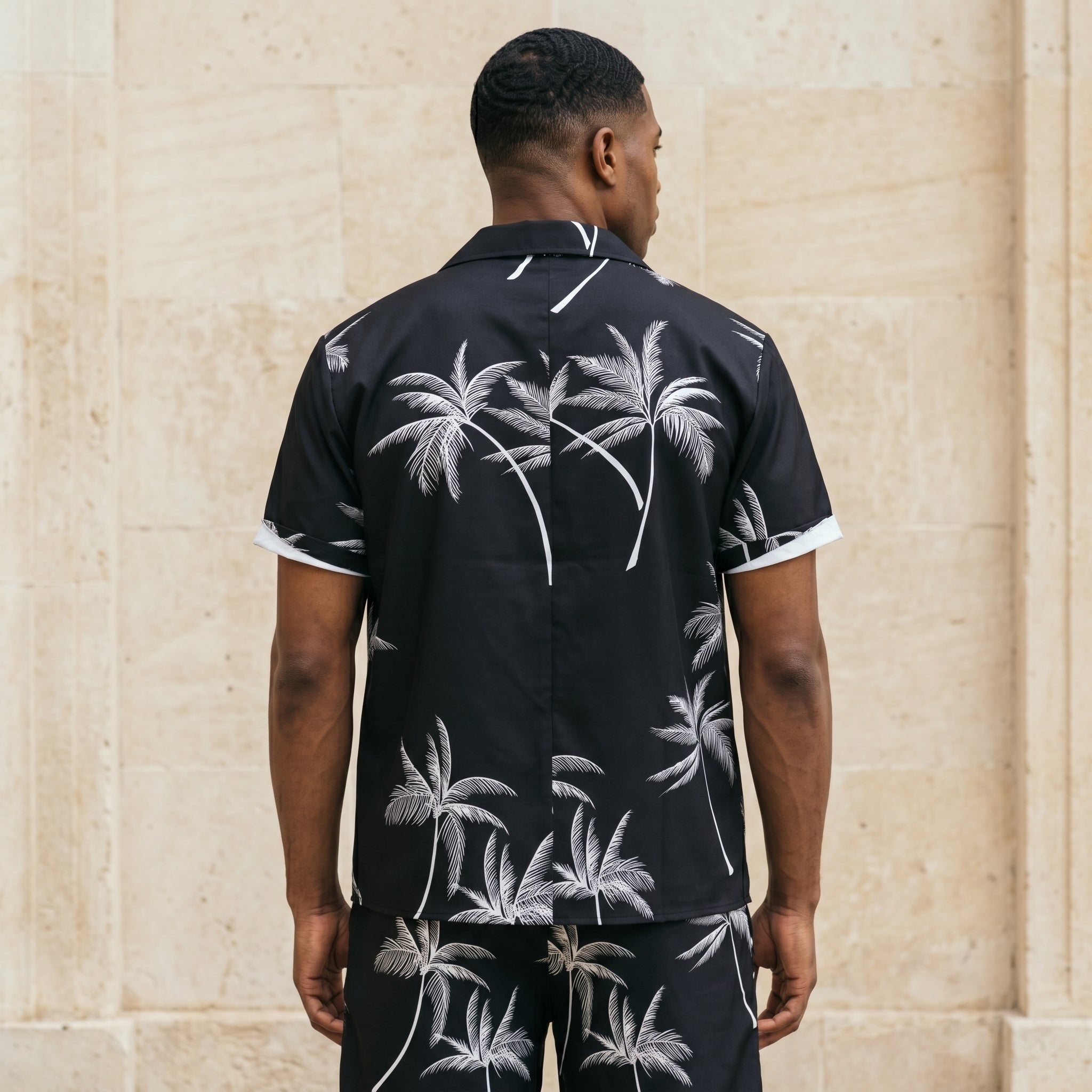 Back view of male model wearing a black palm print short-sleeve shirt with matching black shorts.