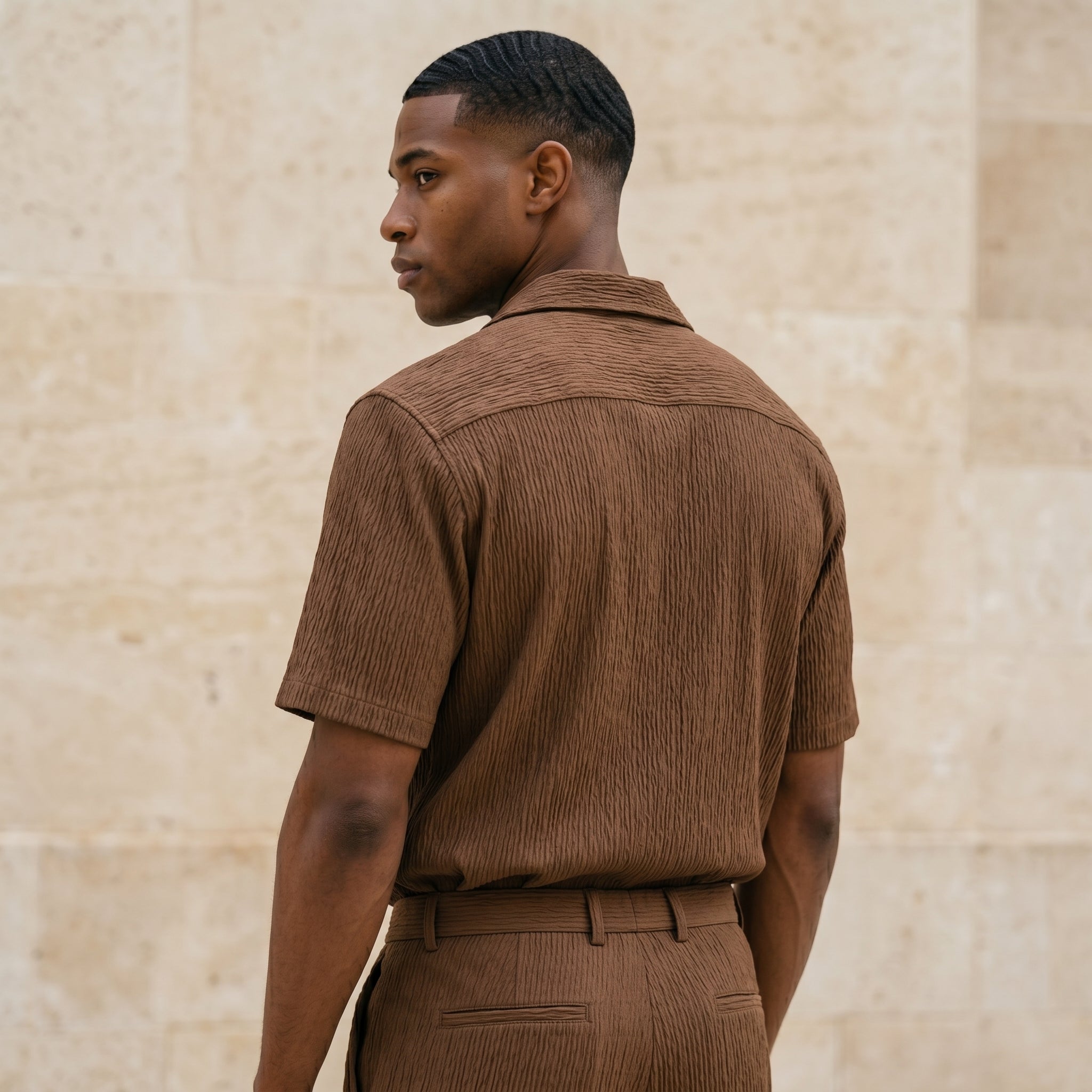 Back view of male model wearing a brown textured short-sleeve shirt with matching pants.