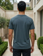 Back view of male model wearing a dark teal blue short-sleeve T-shirt with beige pants.