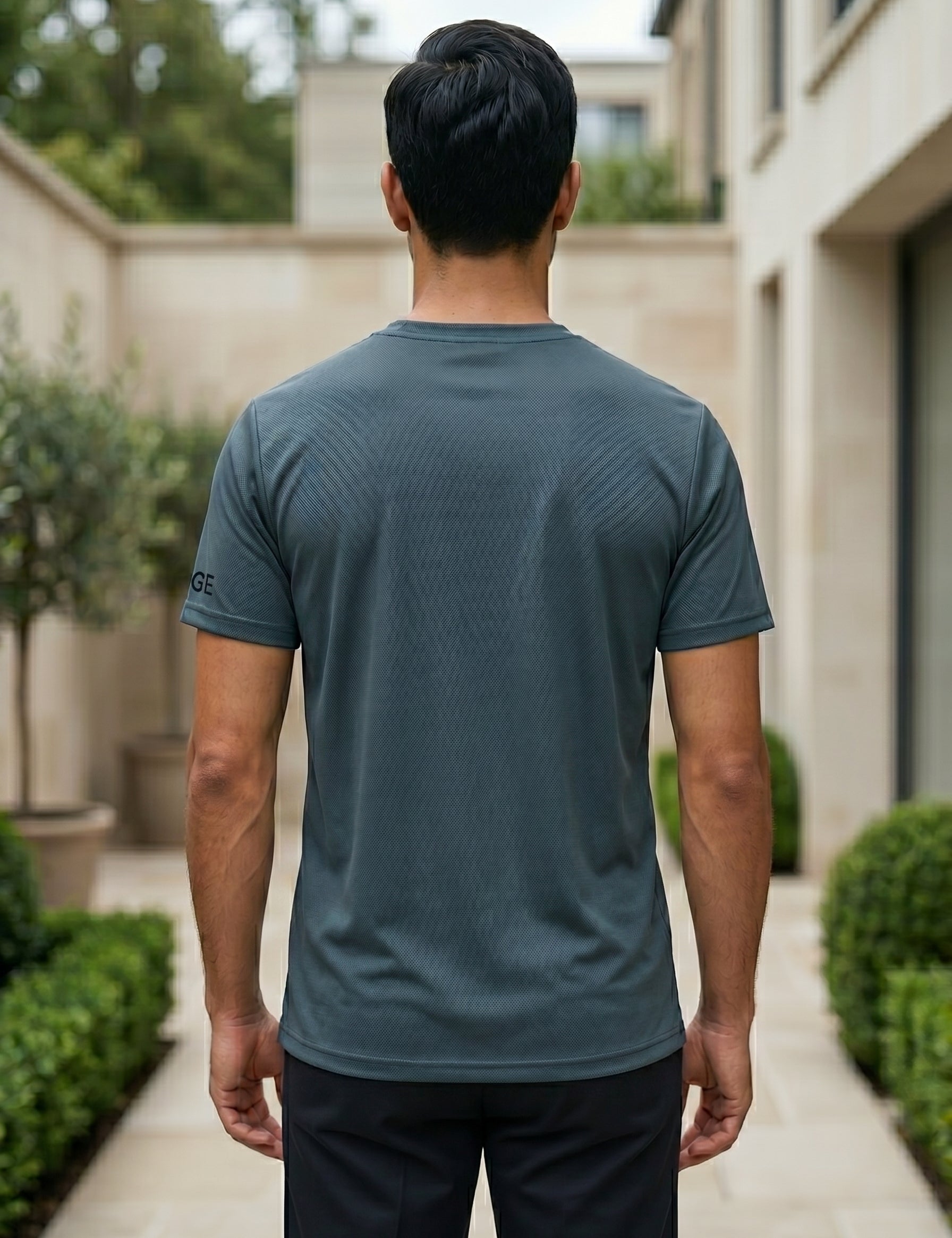 Back view of male model wearing a dark teal blue short-sleeve T-shirt with beige pants.