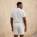 Back view of male model wearing a white textured short-sleeve shirt and matching drawstring summer shorts.
