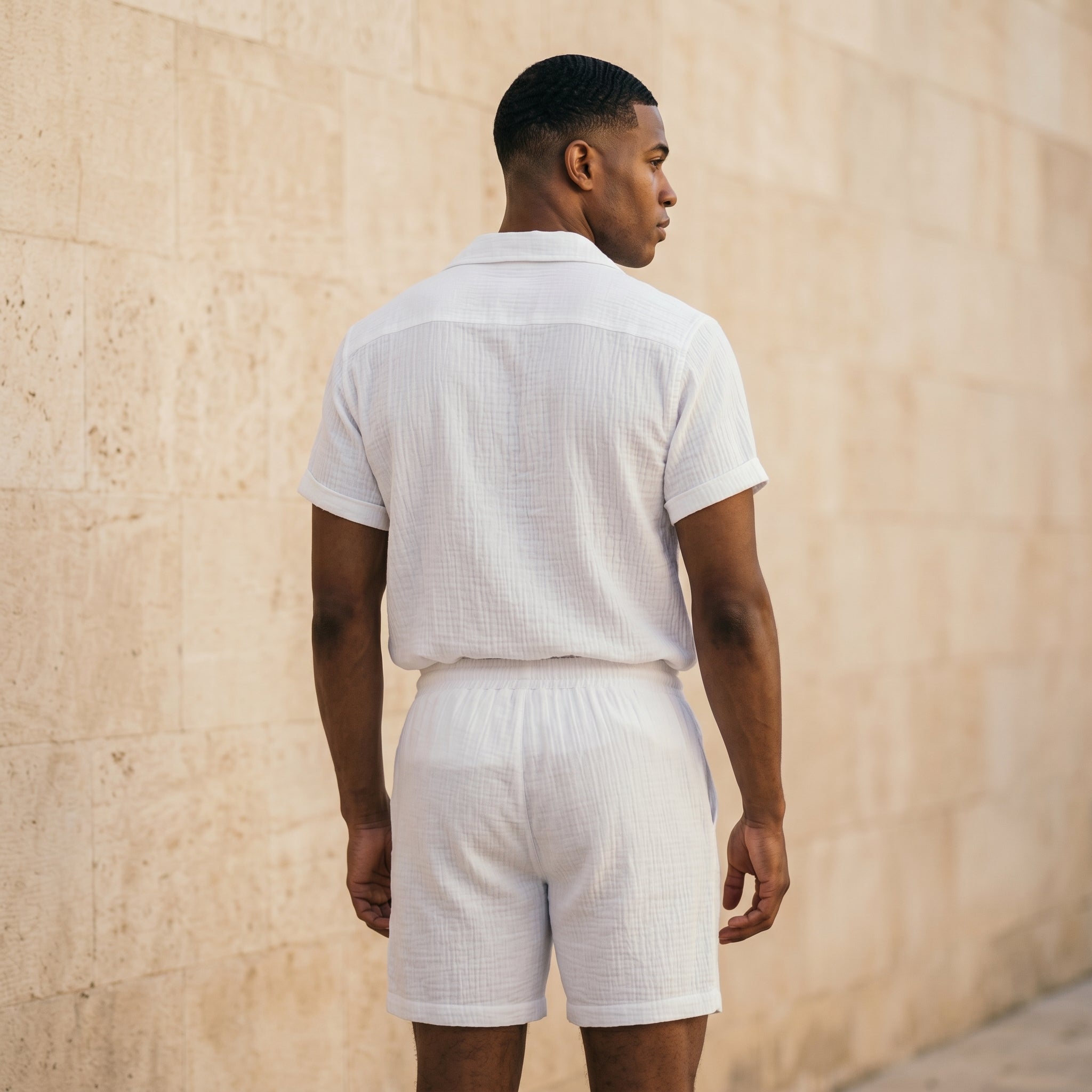 Back view of male model wearing a white textured short-sleeve shirt and matching drawstring summer shorts.
