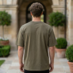Back view of male model wearing an olive green oversized short-sleeve T-shirt with beige pants.