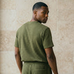 Back view of male model wearing an olive green textured short-sleeve T-shirt and matching shorts.
