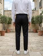 Back view of male model wearing black pleated tailored pants with a white long-sleeve shirt.