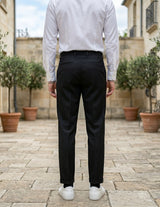 Back view of male model wearing black pleated tailored pants with a white long-sleeve shirt.