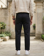 Back view of male model wearing black relaxed-fit casual pants with a beige overshirt and white sneakers.