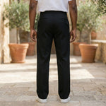Back view of male model wearing black relaxed-fit casual pants with a white short-sleeve shirt.