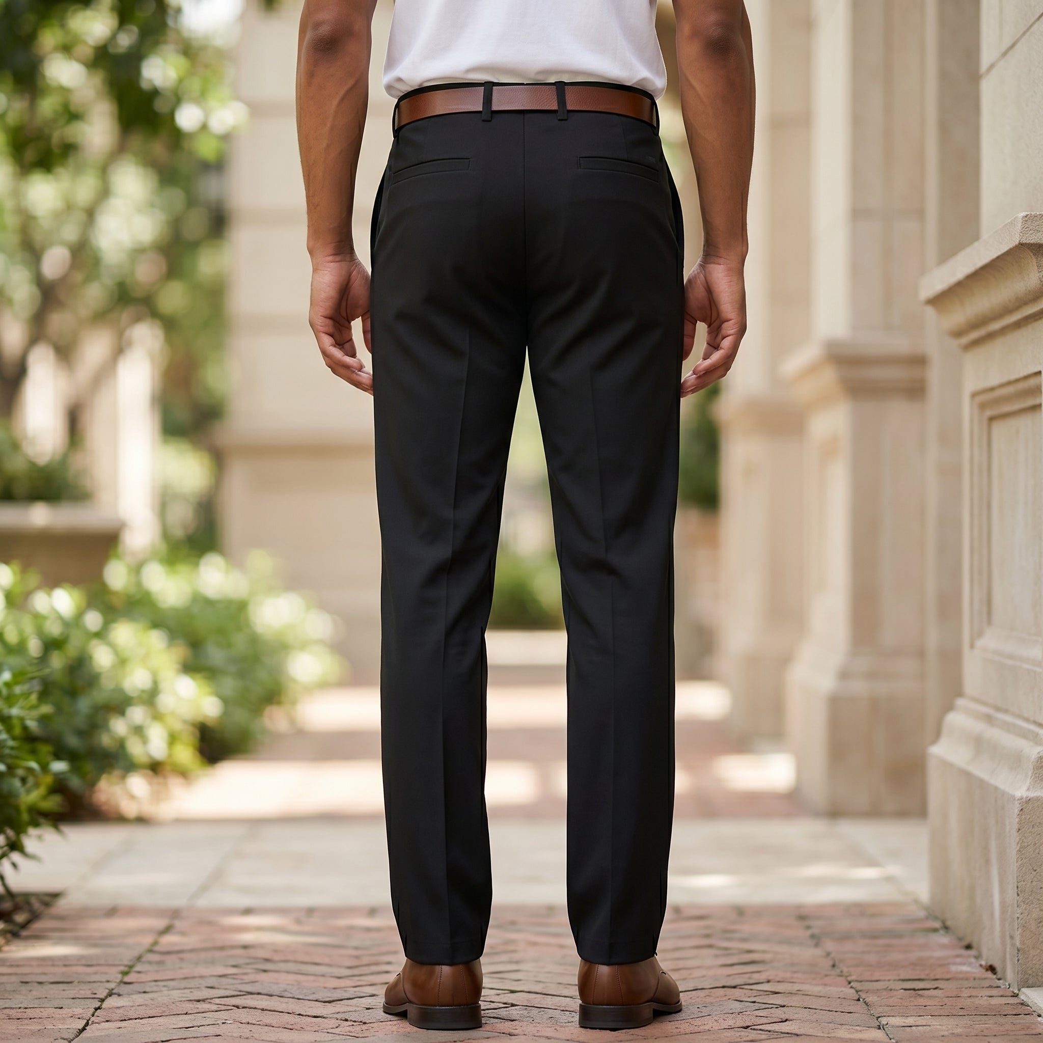 Back view of male model wearing black tailored dress pants with a white long-sleeve shirt.