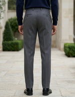 Back view of male model wearing dark gray pleated tailored pants with a navy long-sleeve top.
