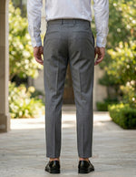 Back view of male model wearing gray pleated tailored pants with a white long-sleeve shirt.