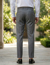 Back view of male model wearing gray pleated tailored pants with a white long-sleeve shirt.