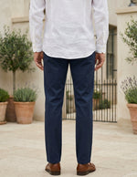 Back view of male model wearing navy tailored pants with a white long-sleeve shirt.