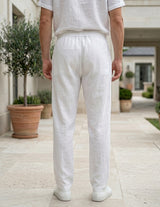 Back view of male model wearing white drawstring relaxed-fit pants with a white short-sleeve shirt.