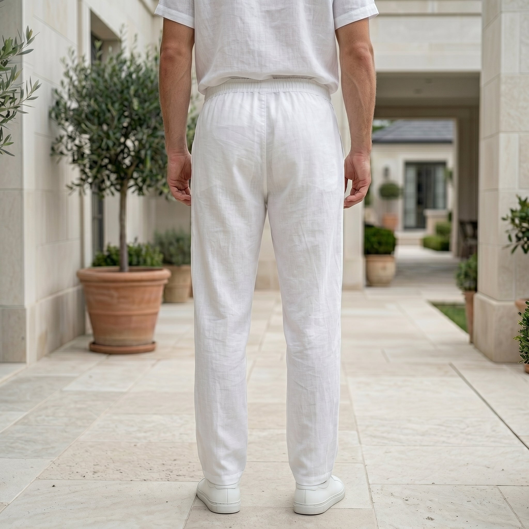 Back view of male model wearing white drawstring relaxed-fit pants with a white short-sleeve shirt.