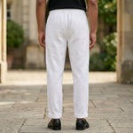 Back view of male model wearing white relaxed-fit pants with a black short-sleeve polo shirt.