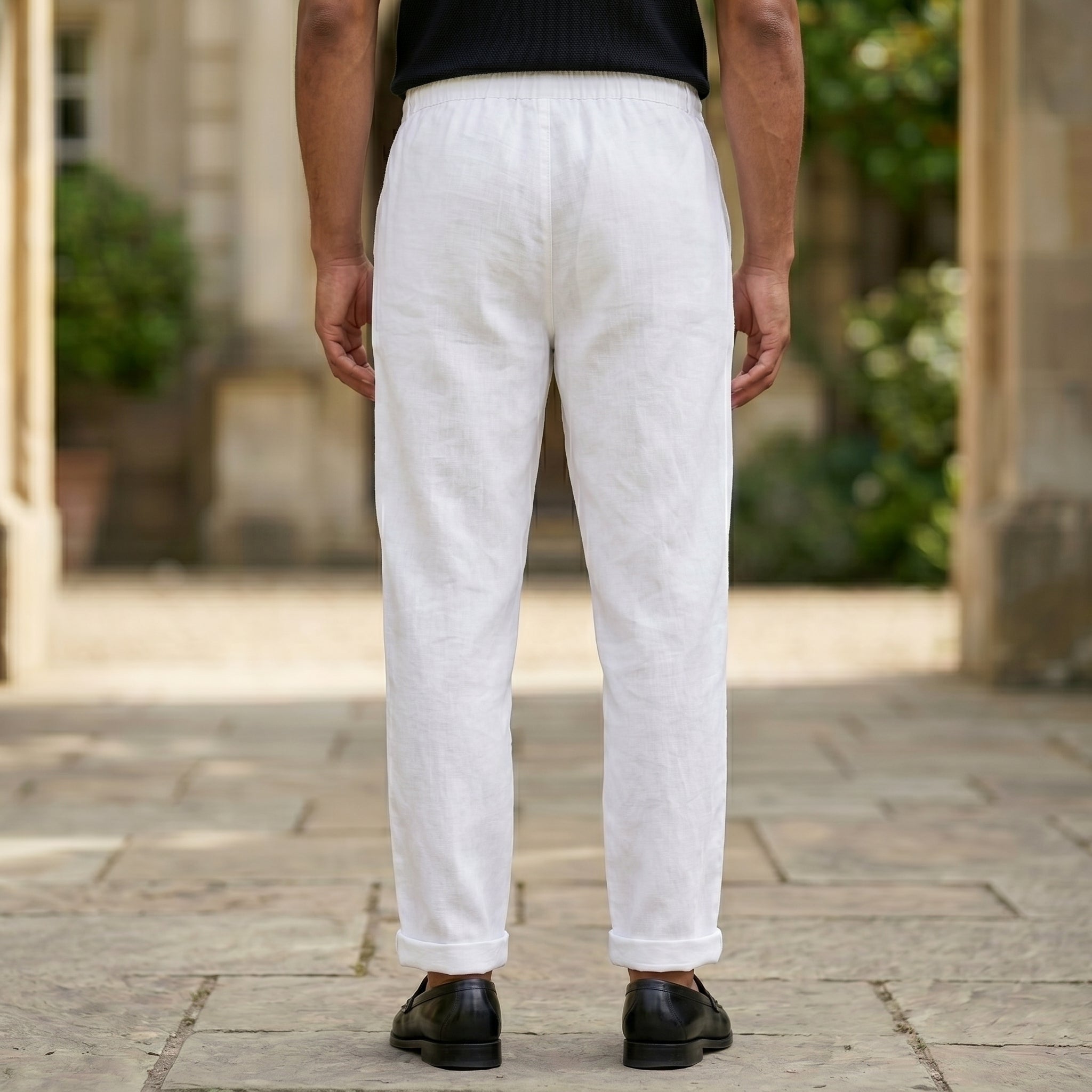 Back view of male model wearing white relaxed-fit pants with a black short-sleeve polo shirt.