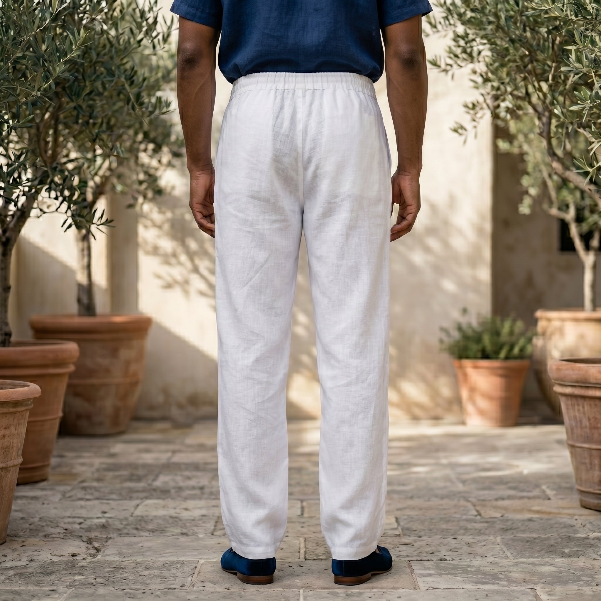 Back view of male model wearing white relaxed-fit pants with a navy short-sleeve button-up shirt.