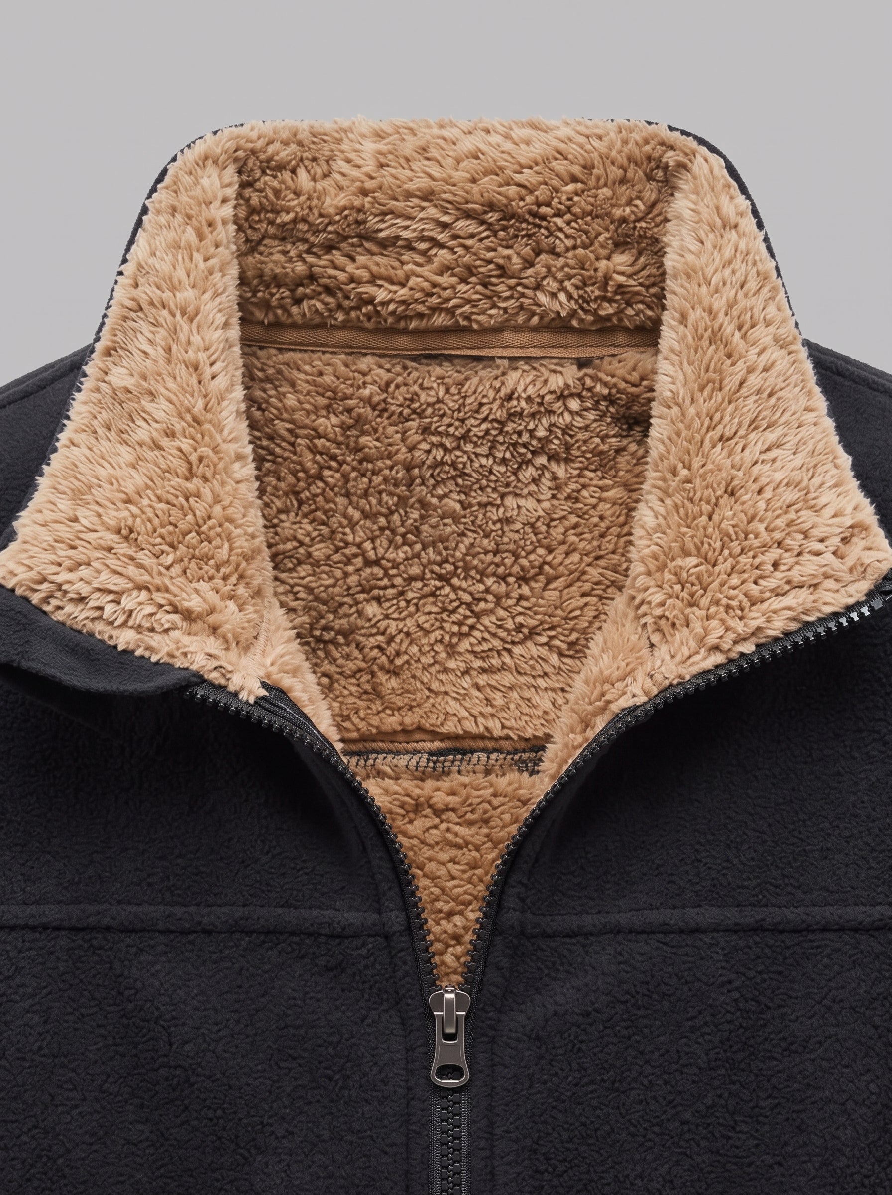Close-up of a black fleece jacket with a thick tan sherpa lining on the collar and inner neck, shown against a neutral gray background.