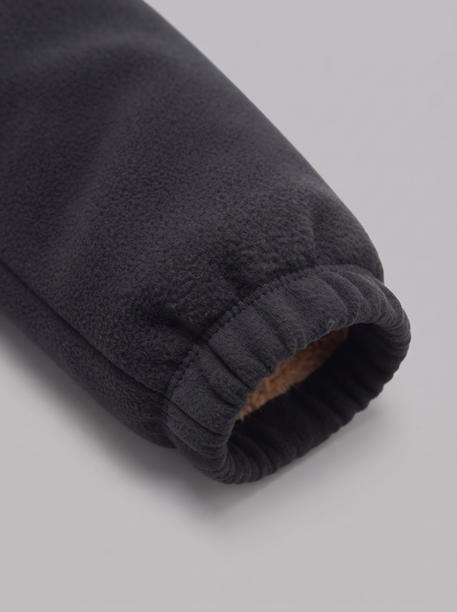 Close-up of a dark charcoal fleece sleeve with a ribbed elastic cuff showing a brown lining, set against a neutral gray background.