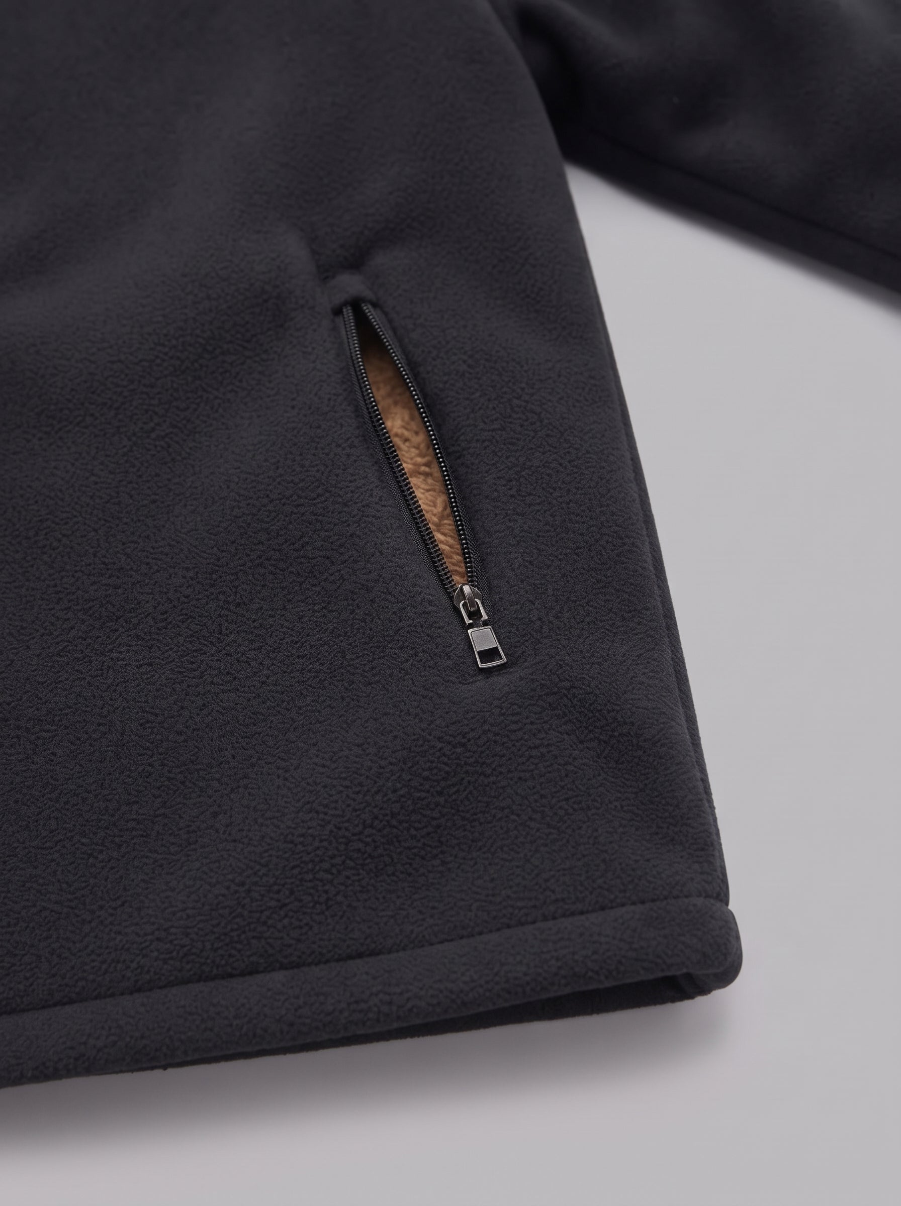 Close-up of a dark charcoal fleece jacket showing a zippered pocket with a brown textured lining and a silver zipper pull, set against a light gray background.