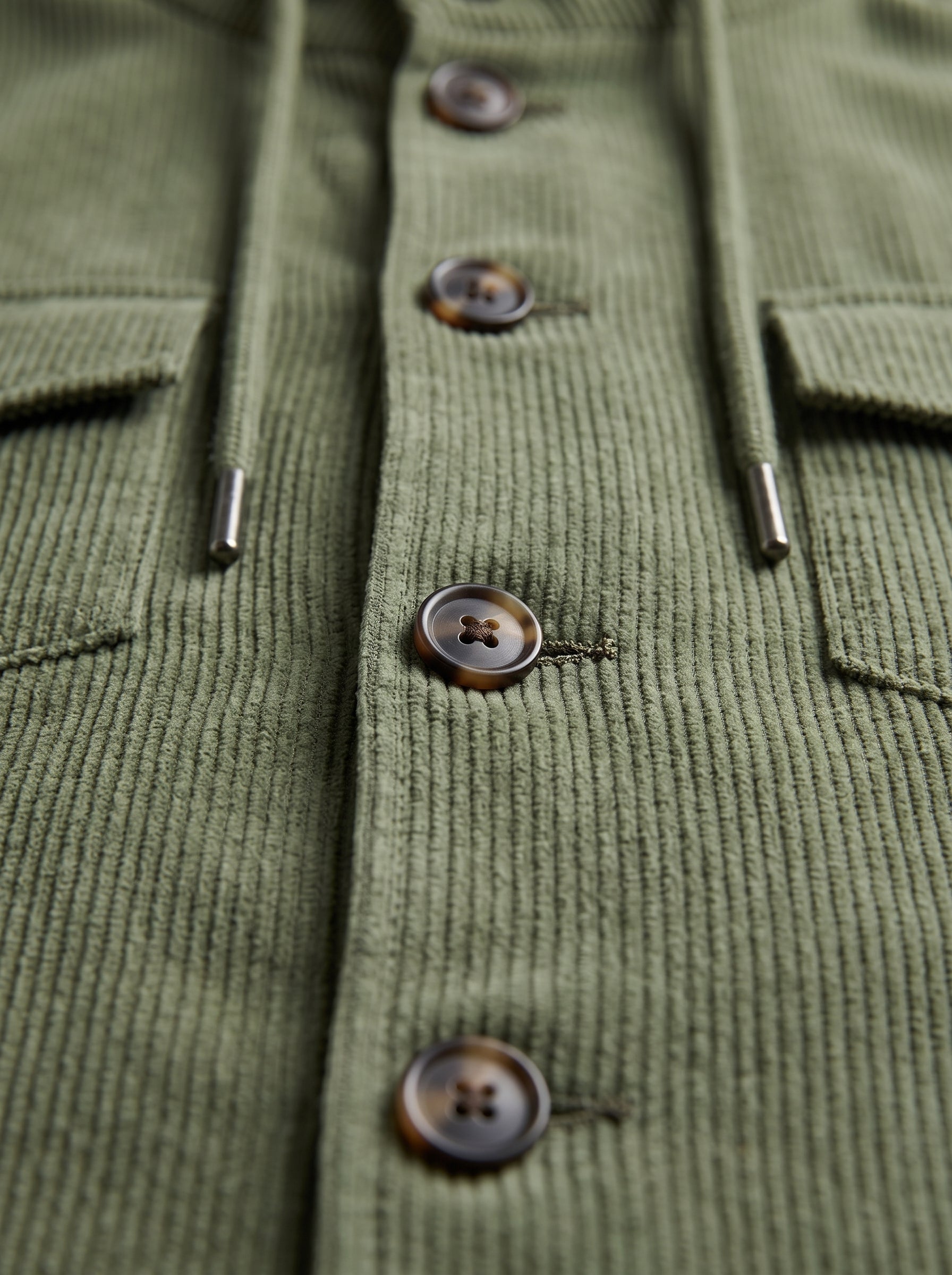 Close-up of an olive green ribbed corduroy shirt jacket with dark brown buttons and a drawstring.