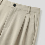 Close-up detail of beige pleated pants waistband with button closure and soft fabric.