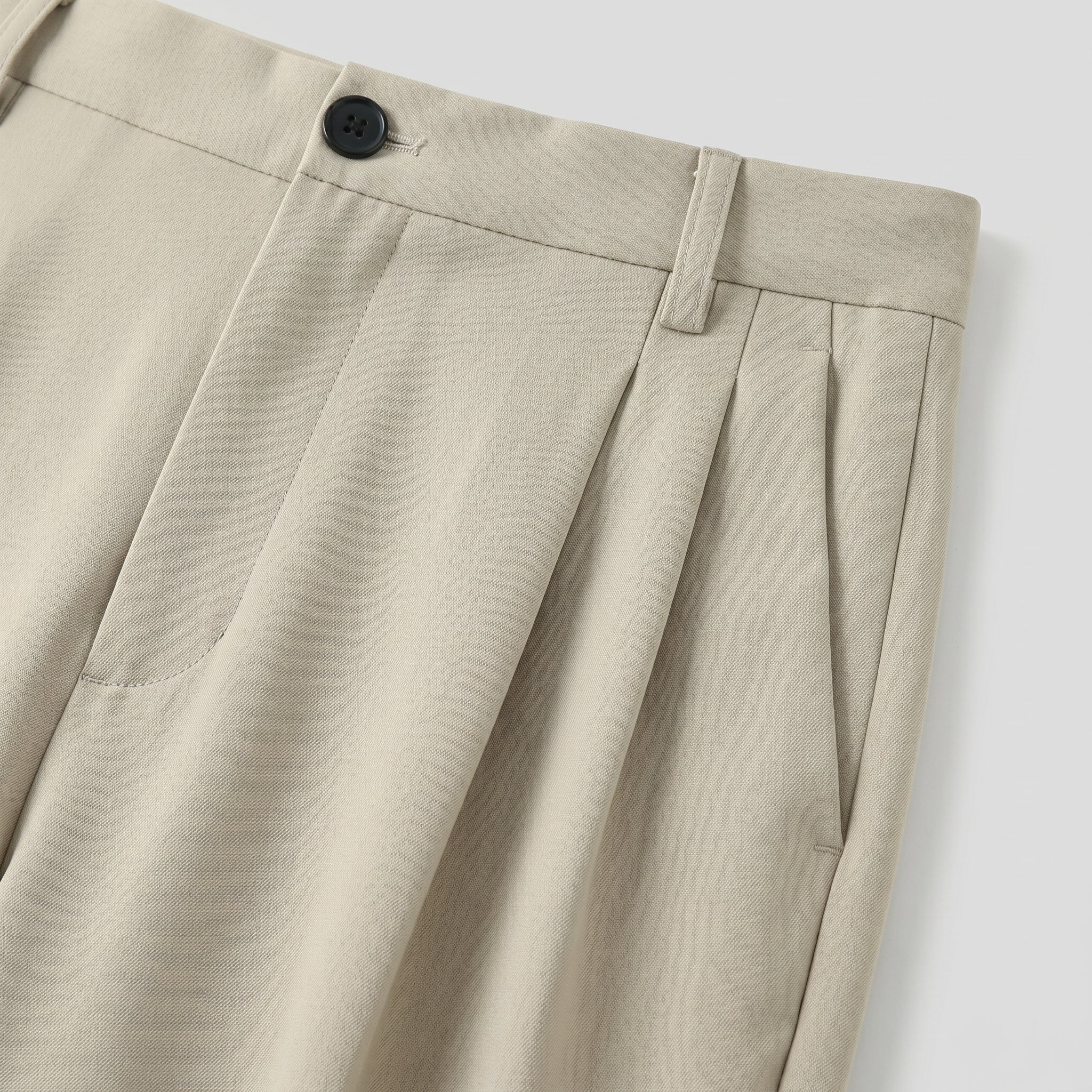 Close-up detail of beige pleated pants waistband with button closure and soft fabric.