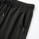 Close-up detail of black jogger pants with elastic waistband, drawstring, and zipper pocket.
