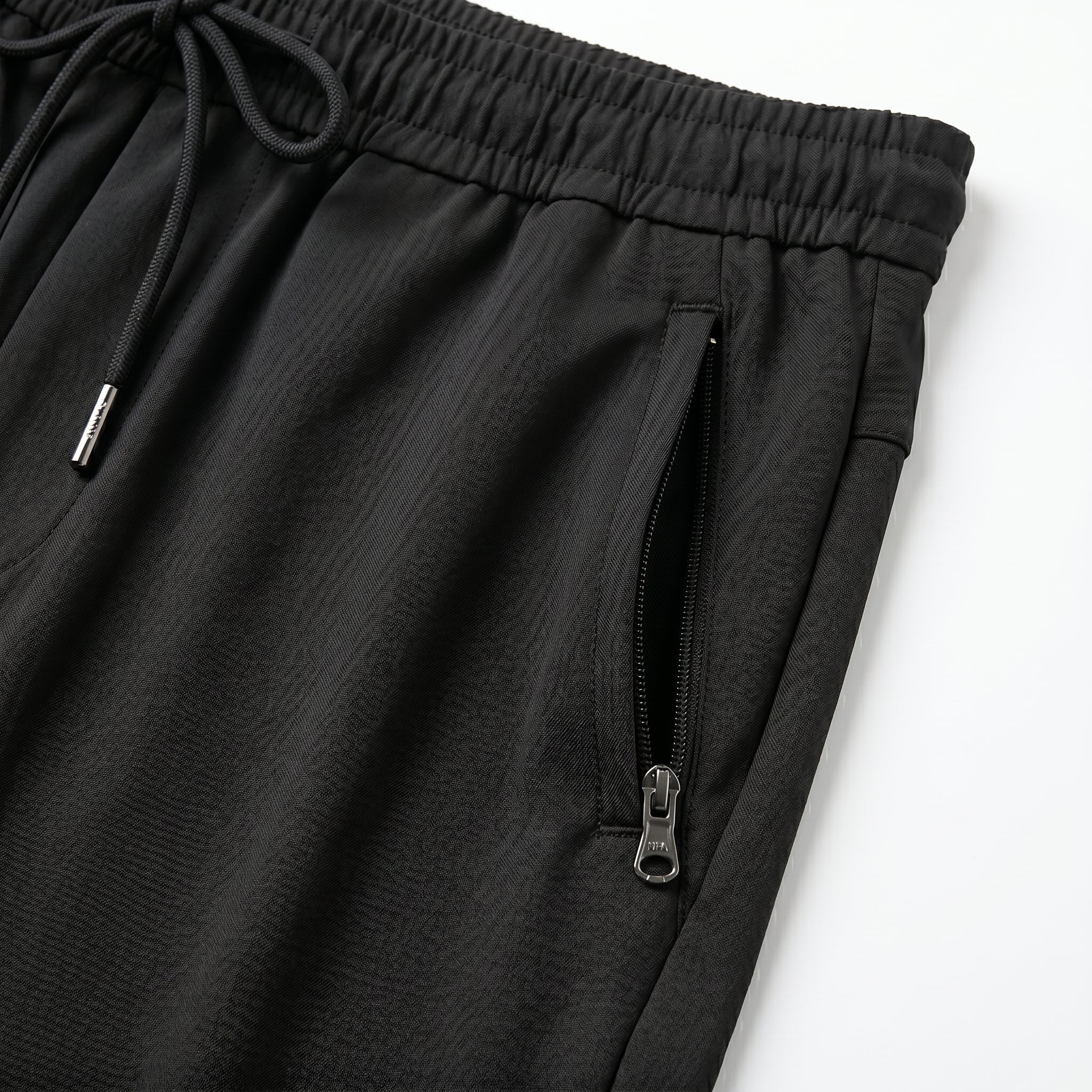 Close-up detail of black jogger pants with elastic waistband, drawstring, and zipper pocket.