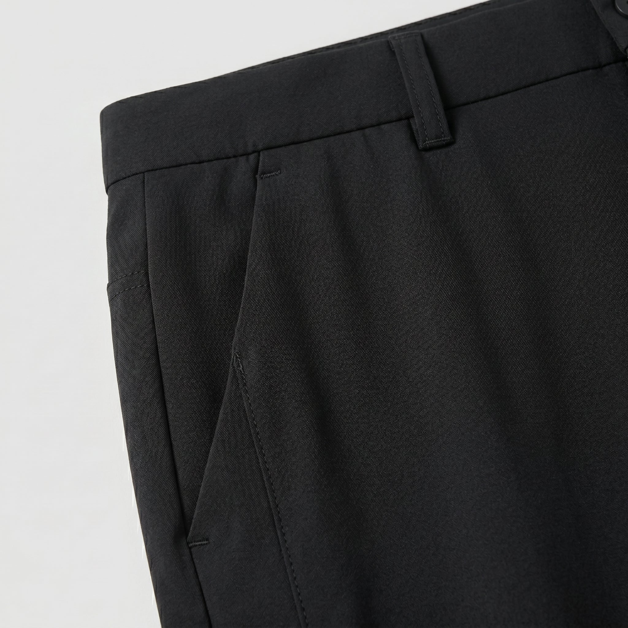Close-up detail of black casual pants waistband, side pocket, and smooth fabric.