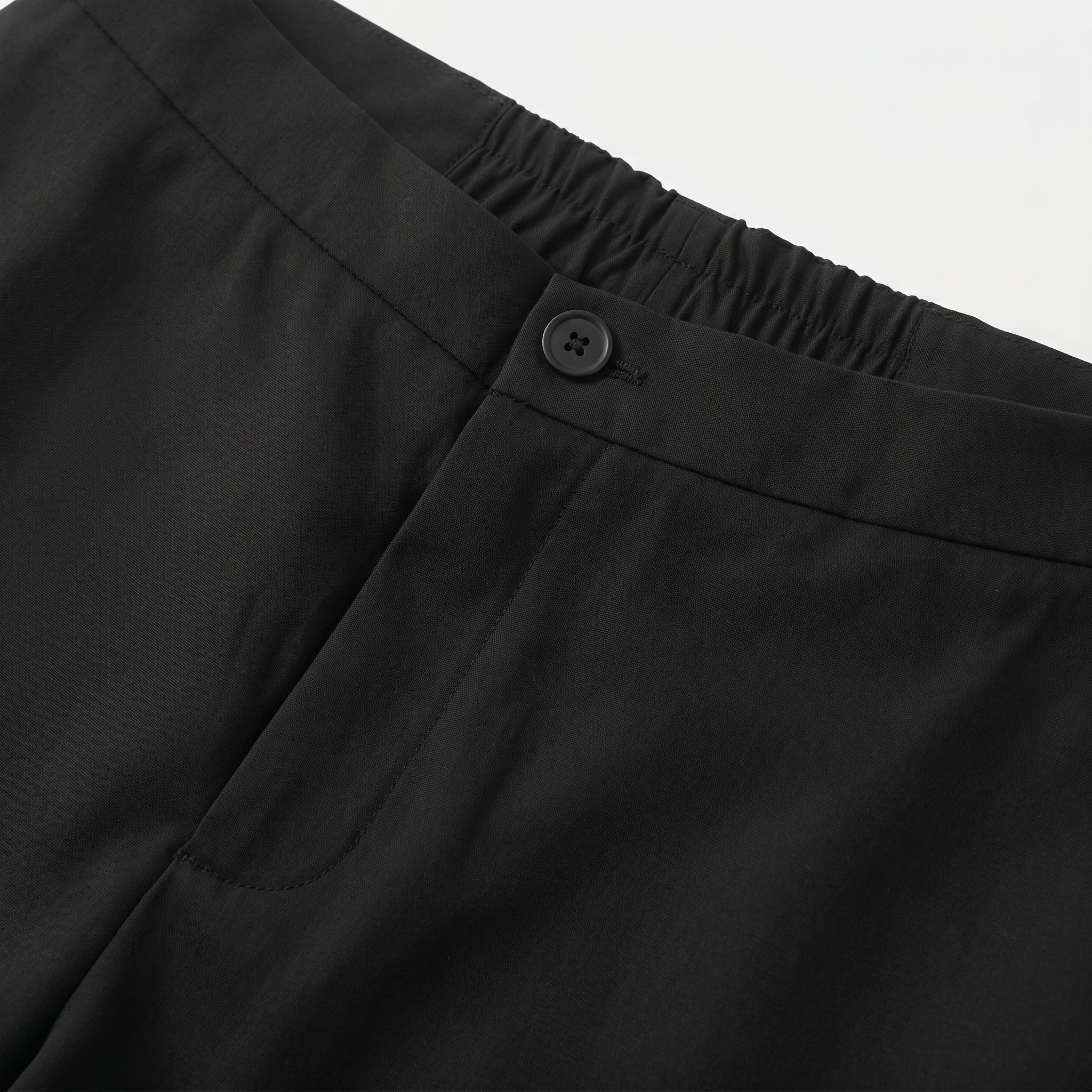 Close-up detail of black casual pants waistband with button closure and smooth fabric.