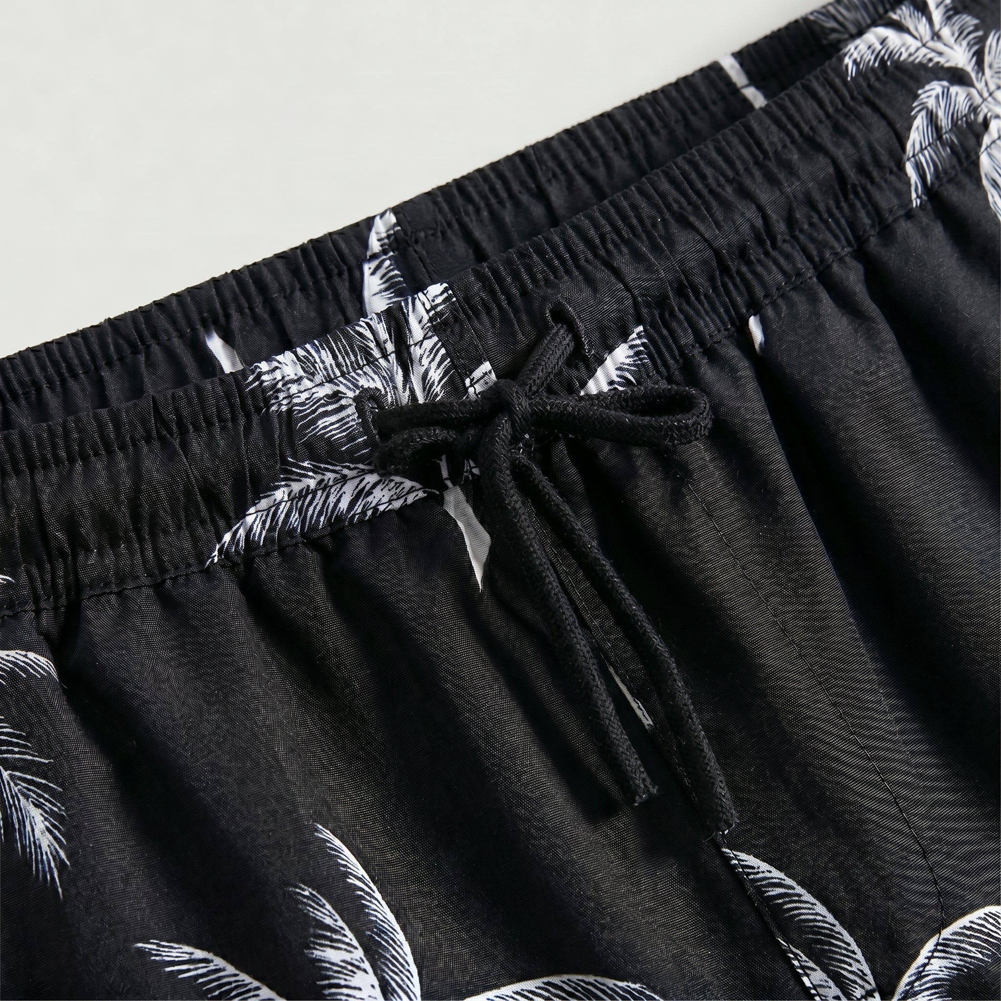 Close-up detail of black palm print drawstring shorts with elastic waistband and black tie.