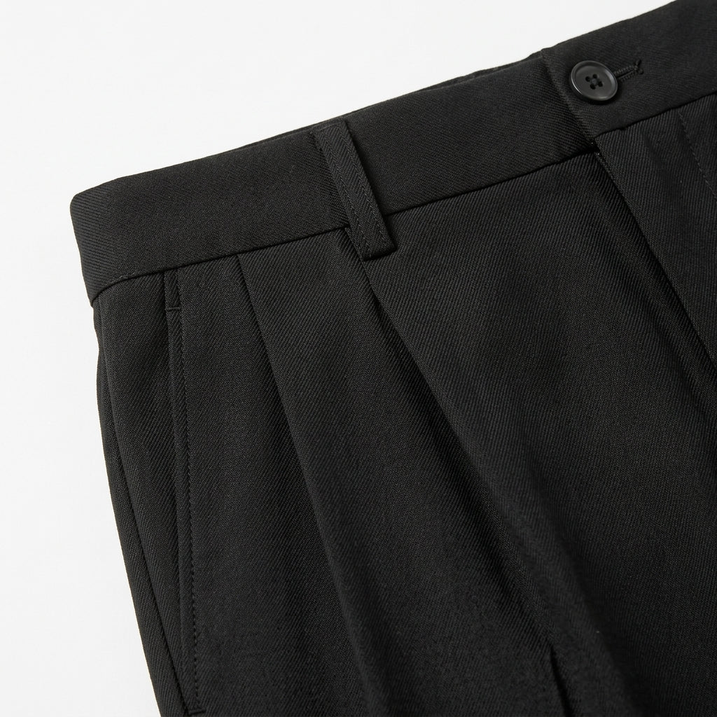 Close-up detail of black pleated pants waistband with belt loops, button closure, and smooth fabric.