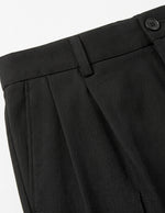 Close-up detail of black pleated pants waistband with belt loops, button closure, and smooth fabric.