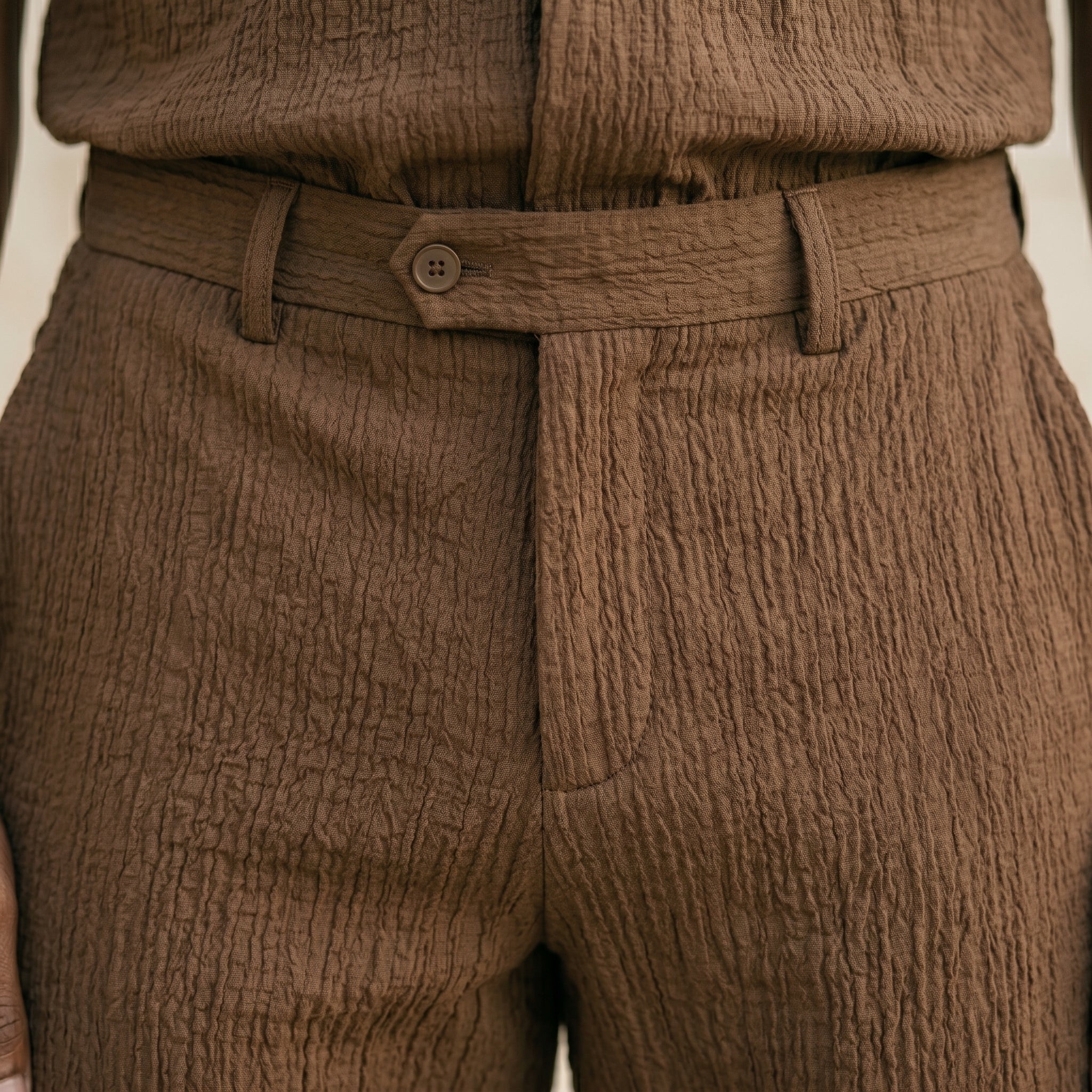 Close-up detail of brown textured pants waistband and front closure.