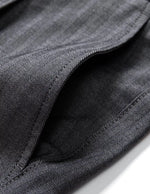 Close-up detail of dark gray pleated pants waistband with belt loops, button closure, and smooth fabric.