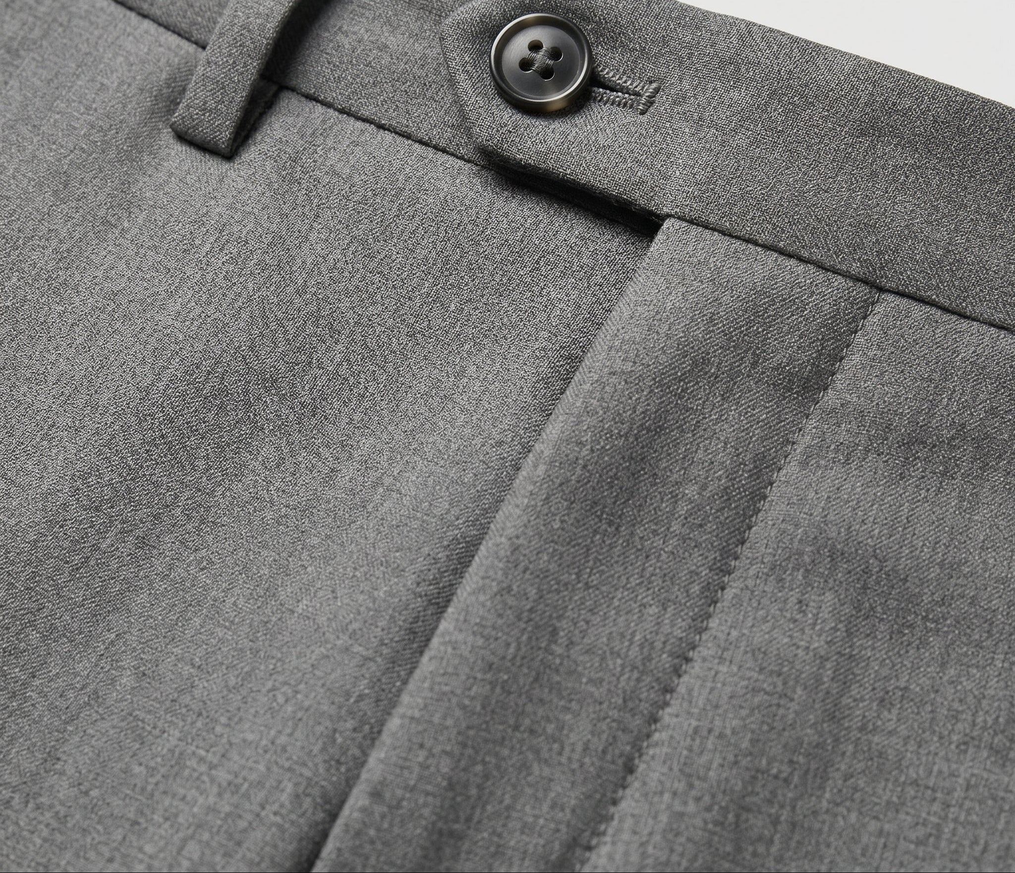 Close-up detail of gray pleated pants waistband with belt loops, button closure, and smooth fabric.