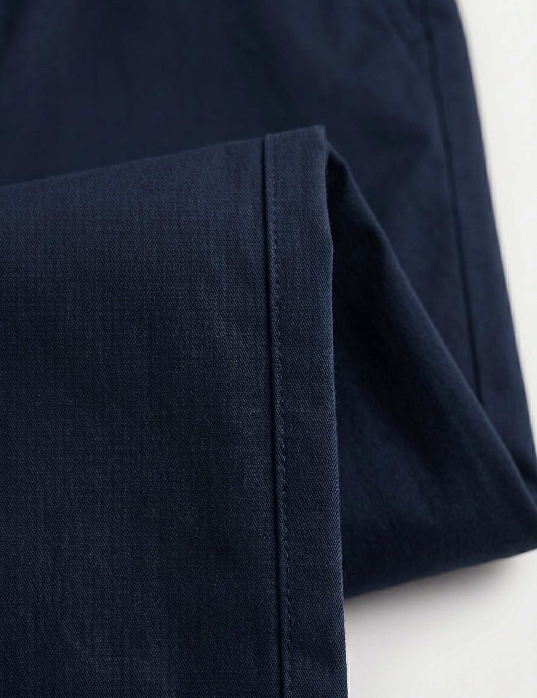 Close-up detail of navy tailored pants waistband with belt loops, button closure, and smooth fabric.