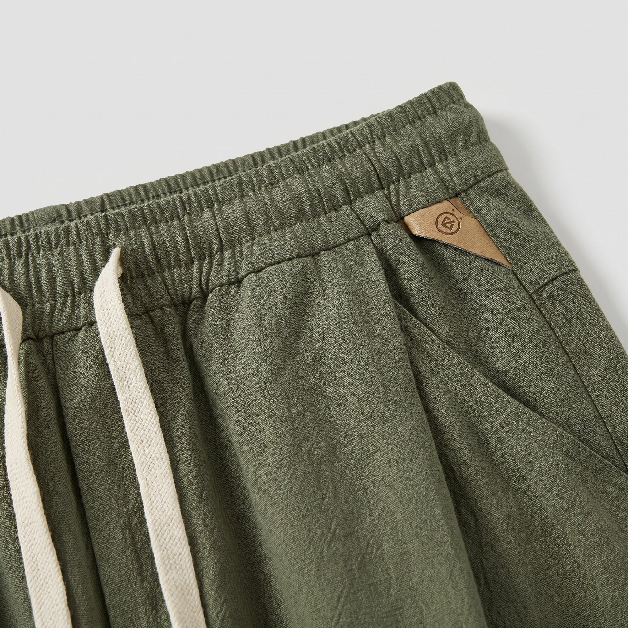 Close-up detail of olive green jogger pants with elastic waistband, drawstring, and side pocket.