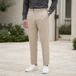 Close-up front view of male model wearing beige pleated casual pants with a relaxed tapered fit.