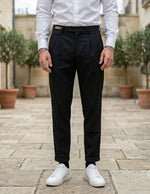 Close-up front view of male model wearing black pleated tailored pants with a relaxed straight-leg fit.